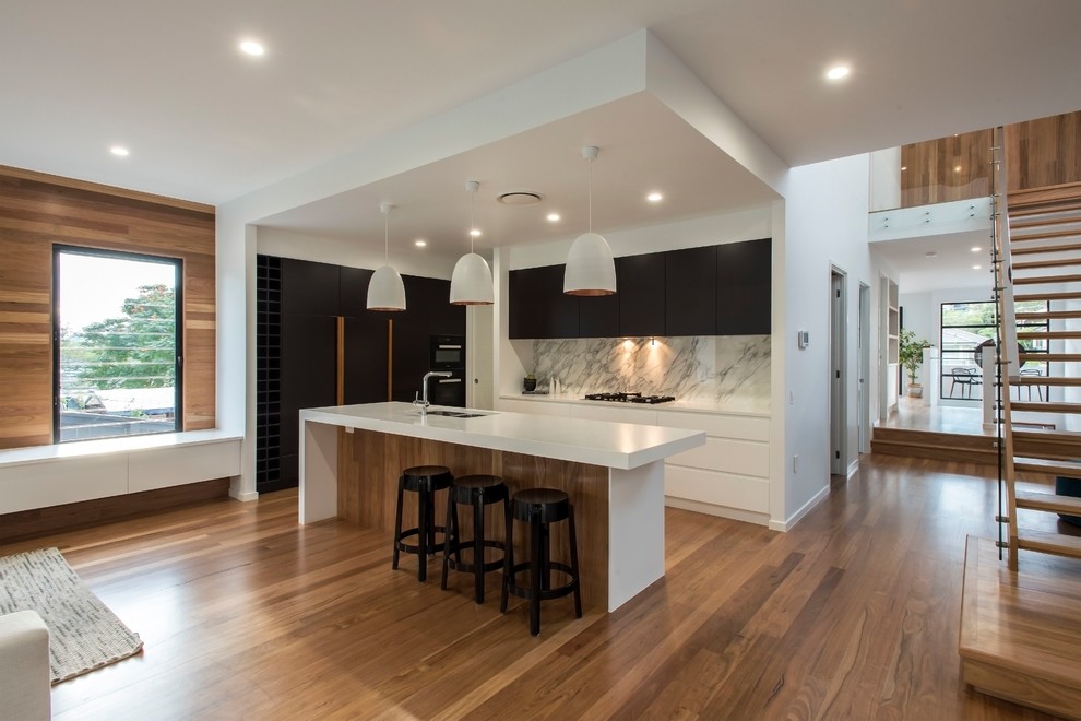 Photo of a contemporary galley kitchen in Brisbane with black cabinets, grey splashback, marble splashback, medium hardwood floors, with island, white benchtop, a double-bowl sink, flat-panel cabinets, black appliances and brown floor.