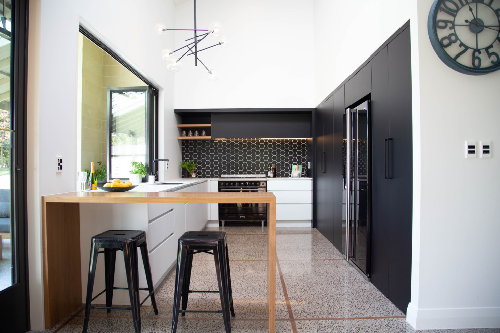 Large contemporary u-shaped kitchen in Other with an undermount sink, flat-panel cabinets, solid surface benchtops, black splashback, ceramic splashback, black appliances, concrete floors, with island, white benchtop and multi-coloured floor.