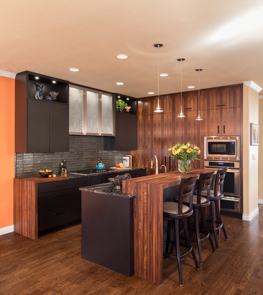 This is an example of a contemporary galley open plan kitchen in Denver with flat-panel cabinets, black cabinets, metallic splashback, matchstick tile splashback, stainless steel appliances, dark hardwood floors, with island and brown floor.