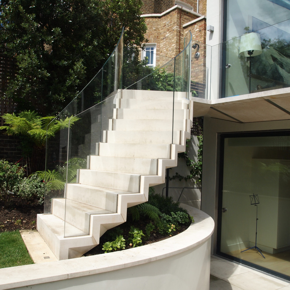 Photo of a modern floating glass railing staircase in Other with limestone treads and limestone risers.