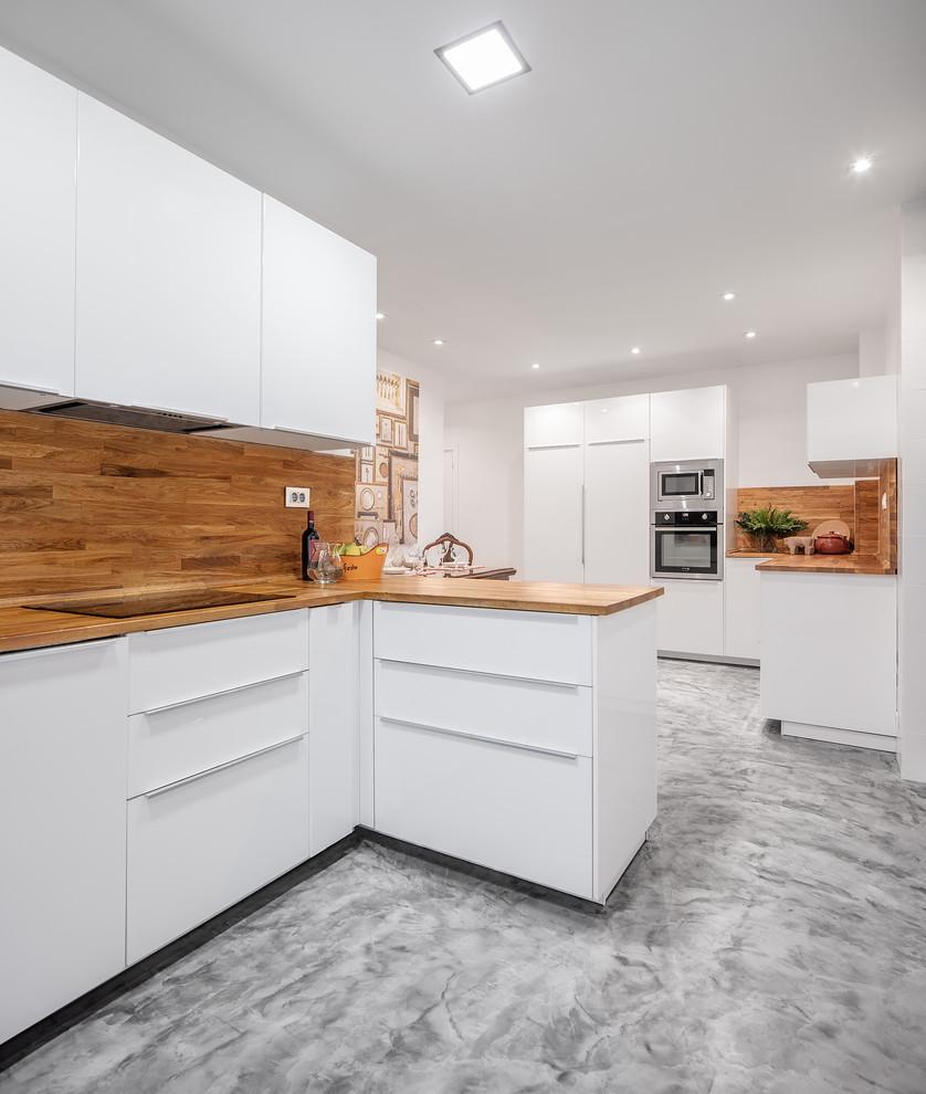 Mid-sized eclectic l-shaped eat-in kitchen in Bilbao with an integrated sink, flat-panel cabinets, white cabinets, wood benchtops, brown splashback, timber splashback, panelled appliances, concrete floors, a peninsula, grey floor and brown benchtop.