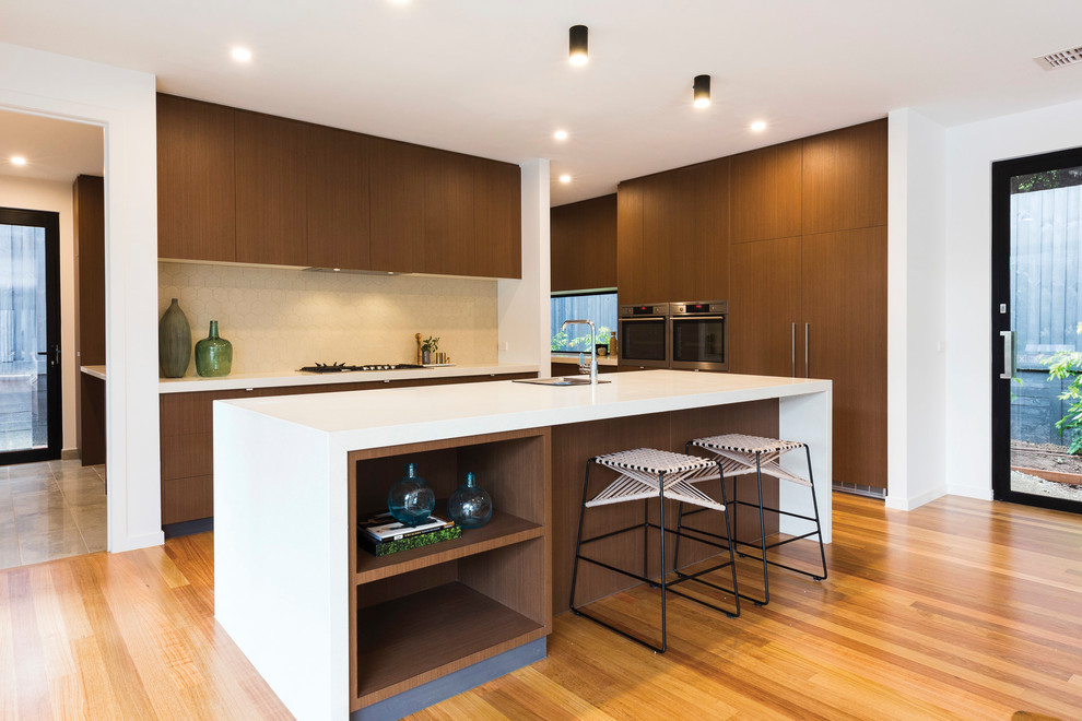 Photo of a contemporary kitchen in Melbourne with a single-bowl sink, flat-panel cabinets, dark wood cabinets, beige splashback, medium hardwood floors, with island, white benchtop and panelled appliances.