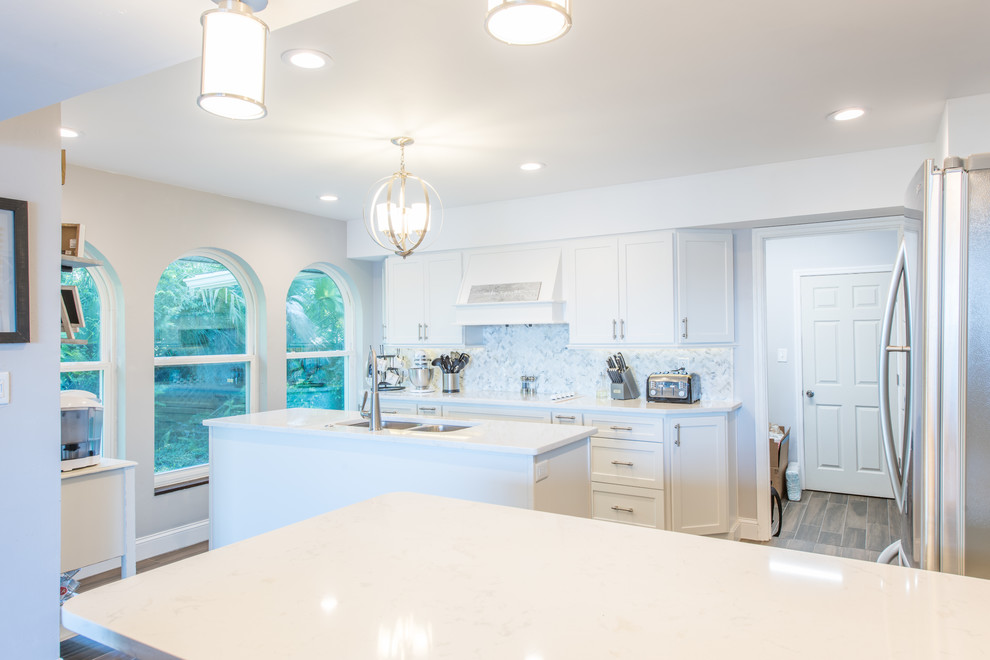 Example of a large transitional u-shaped porcelain tile and brown floor eat-in kitchen design with an undermount sink, shaker cabinets, white cabinets, quartz countertops, white backsplash, marble backsplash, stainless steel appliances and two islands