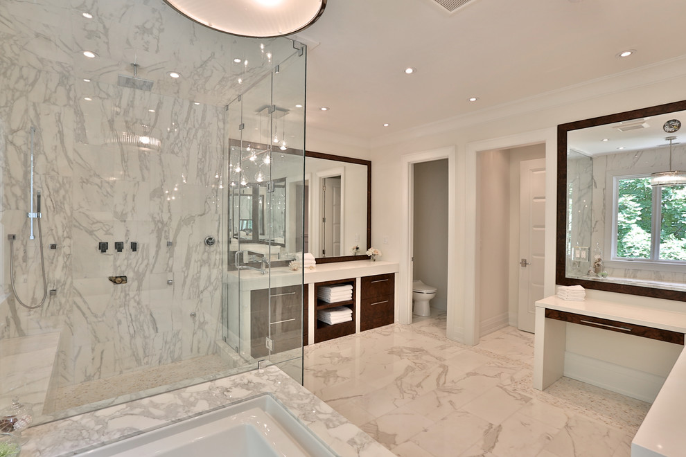This is an example of a large modern master bathroom in Toronto with flat-panel cabinets, dark wood cabinets, a drop-in tub, a corner shower, gray tile, white tile, stone tile, white walls, marble floors, an undermount sink, a one-piece toilet, quartzite benchtops, white floor and a hinged shower door.