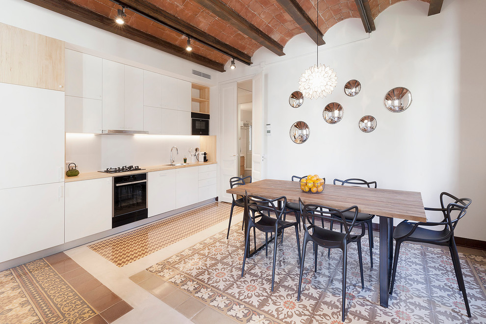 Photo of a large mediterranean single-wall open plan kitchen in Barcelona with an undermount sink, flat-panel cabinets, white cabinets, wood benchtops, white splashback, ceramic floors, no island, multi-coloured floor and black appliances.