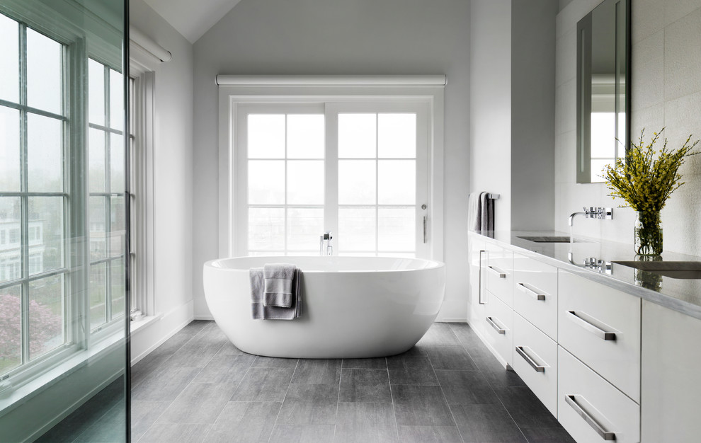 Inspiration for a mid-sized beach style master bathroom in New York with grey floor, flat-panel cabinets, white cabinets, a freestanding tub, white tile, white walls, an undermount sink, an alcove shower, porcelain floors, a hinged shower door and grey benchtops.