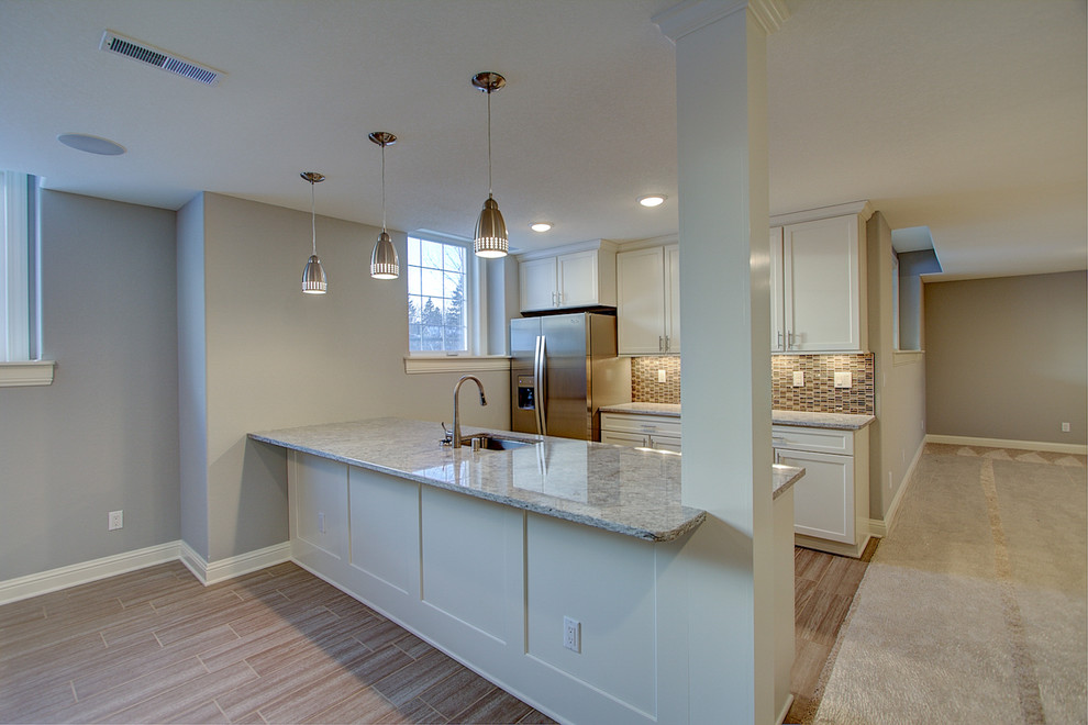 Photo of a large transitional galley seated home bar in Milwaukee with a drop-in sink, recessed-panel cabinets, white cabinets, granite benchtops, multi-coloured splashback, ceramic splashback and porcelain floors.