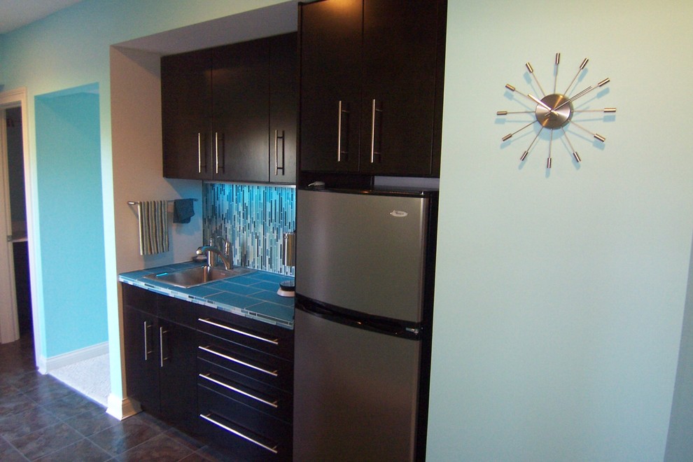 Design ideas for a small modern single-wall wet bar in Cincinnati with a drop-in sink, flat-panel cabinets, black cabinets, tile benchtops, blue splashback and glass tile splashback.