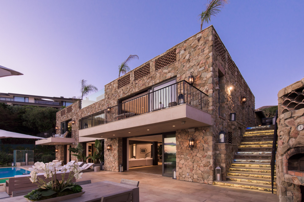 Inspiration for a large mediterranean two-storey brown house exterior in Los Angeles with stone veneer, a flat roof and a tile roof.