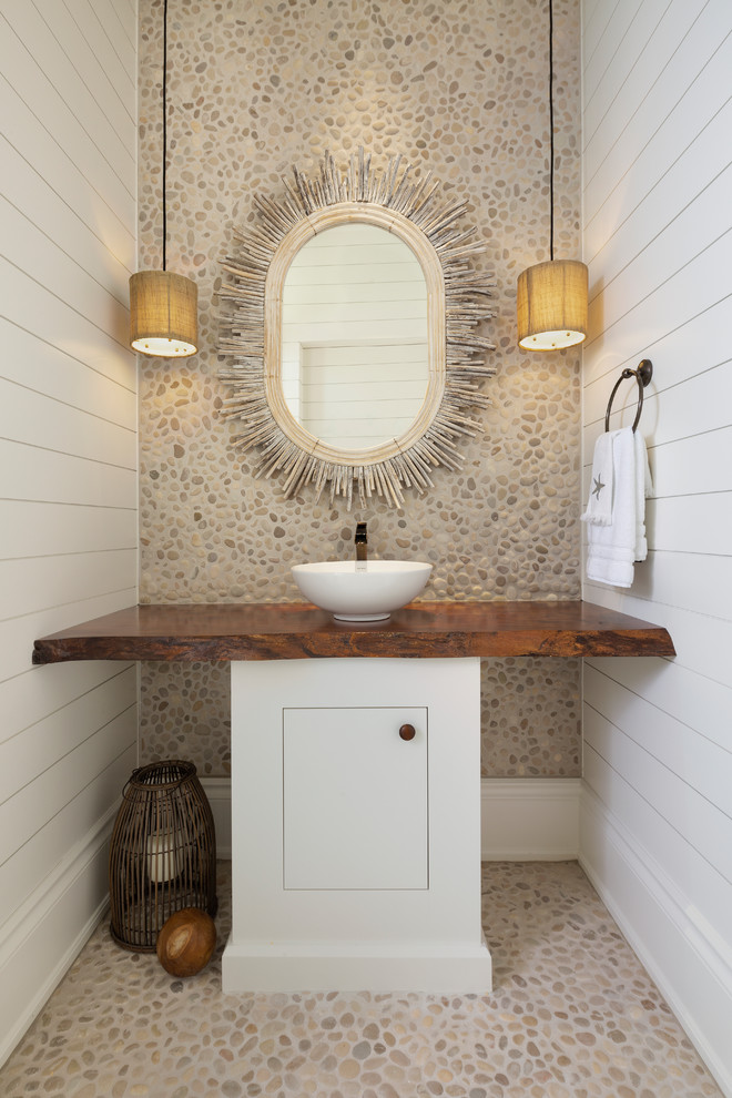 This is an example of a beach style powder room in Miami with flat-panel cabinets, white cabinets, beige tile, pebble tile, white walls, pebble tile floors, a vessel sink, wood benchtops, beige floor and brown benchtops.