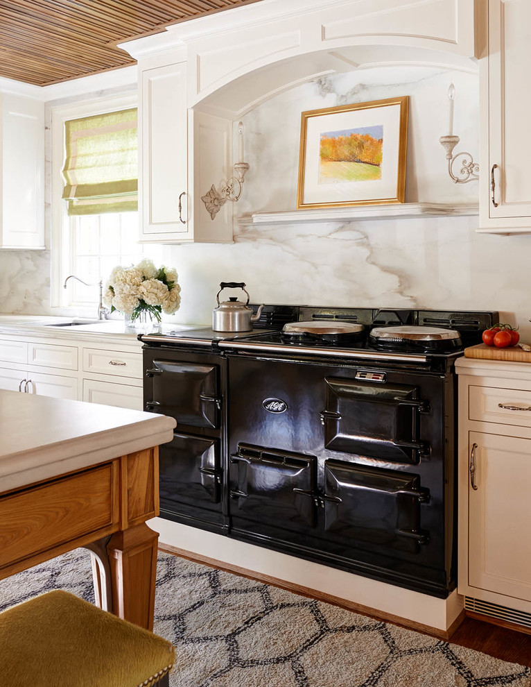 Example of a large classic u-shaped medium tone wood floor enclosed kitchen design in Charlotte with a drop-in sink, recessed-panel cabinets, white cabinets, marble countertops, white backsplash, stone slab backsplash, black appliances and no island