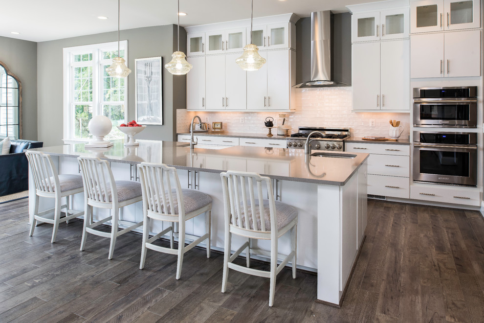 Transitional galley open plan kitchen in DC Metro with a farmhouse sink, flat-panel cabinets, white cabinets, white splashback, subway tile splashback, stainless steel appliances, dark hardwood floors, with island and brown floor.