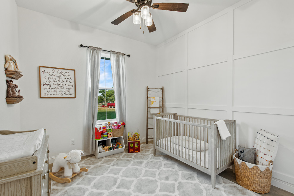 Ejemplo de habitación de bebé neutra blanca campestre de tamaño medio con paredes blancas, suelo de cemento, suelo beige y panelado