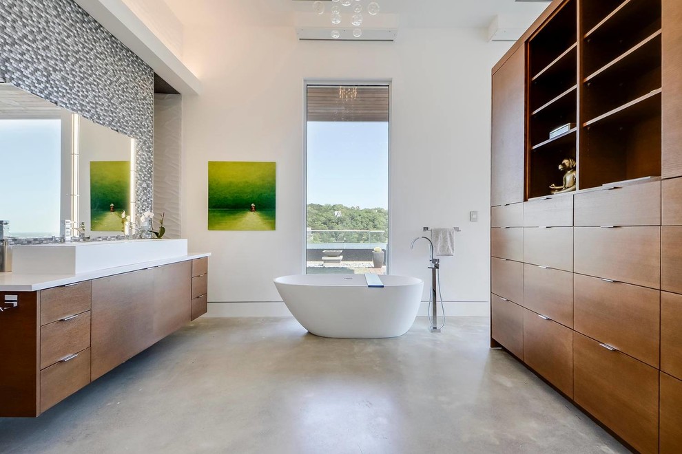 Photo of a contemporary master bathroom in Austin with flat-panel cabinets, medium wood cabinets, a freestanding tub, multi-coloured tile, mosaic tile, white walls and concrete floors.