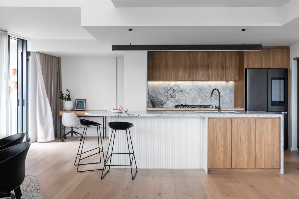 Inspiration for a mid-sized contemporary galley open plan kitchen in Melbourne with an undermount sink, flat-panel cabinets, medium wood cabinets, marble benchtops, grey splashback, marble splashback, black appliances, medium hardwood floors, with island, brown floor and grey benchtop.
