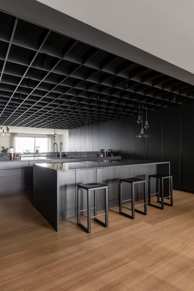 Idéer för att renovera ett mycket stort funkis svart svart kök, med en nedsänkt diskho, släta luckor, grå skåp, granitbänkskiva, svart stänkskydd, svarta vitvaror, ljust trägolv, en köksö och beiget golv