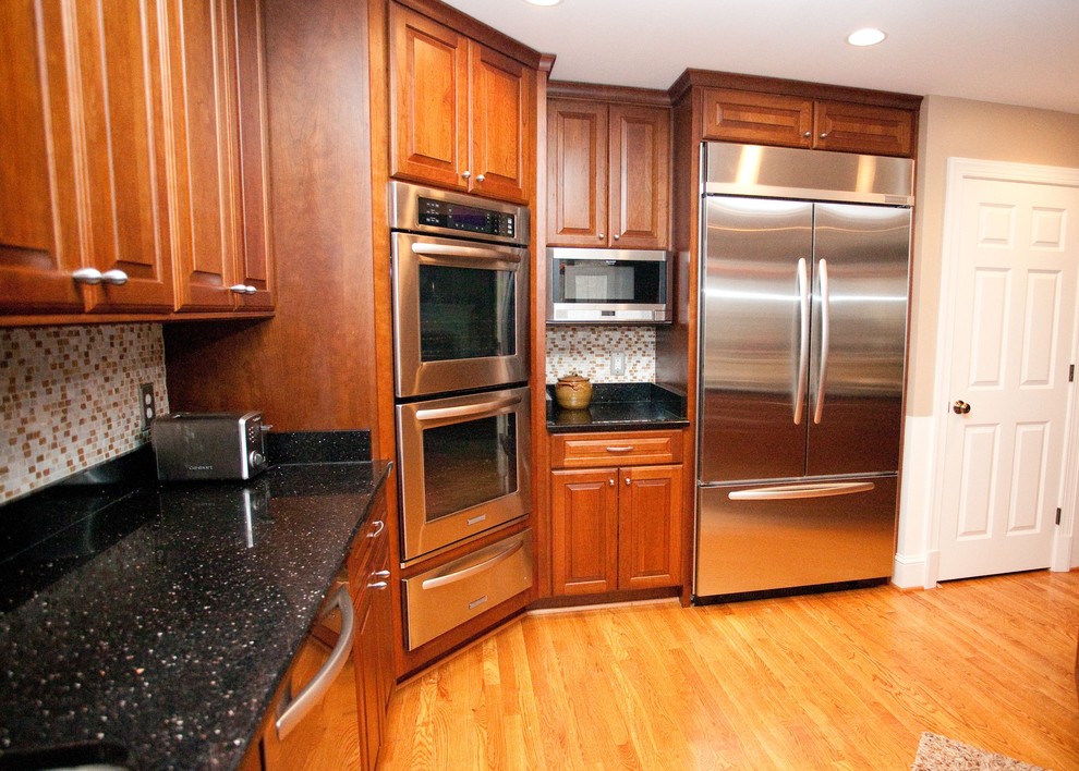 Photo of a mid-sized modern l-shaped eat-in kitchen in DC Metro with a double-bowl sink, raised-panel cabinets, dark wood cabinets, multi-coloured splashback, stainless steel appliances, medium hardwood floors and with island.