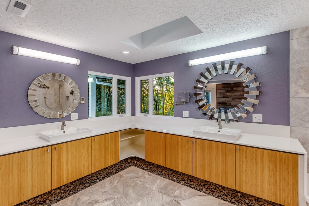 На фото: большая главная ванная комната в стиле модернизм с плоскими фасадами, светлыми деревянными фасадами, угловой ванной, угловым душем, унитазом-моноблоком, серой плиткой, каменной плиткой, фиолетовыми стенами, полом из травертина, монолитной раковиной, столешницей из искусственного кварца, серым полом, открытым душем и белой столешницей с