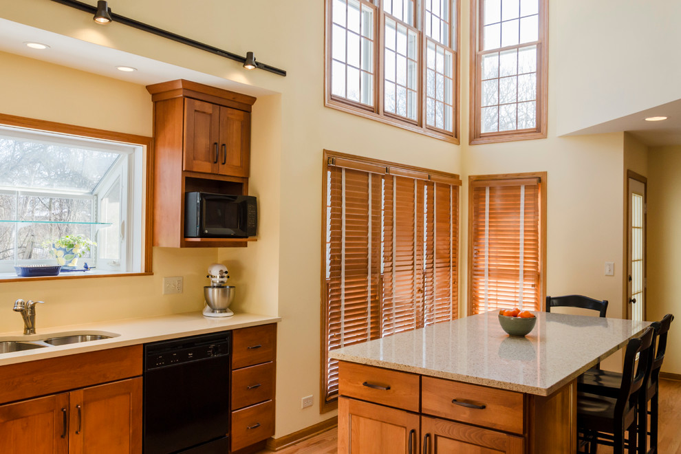 Traditional l-shaped eat-in kitchen in Chicago with an undermount sink, flat-panel cabinets, light wood cabinets, quartz benchtops, black appliances and light hardwood floors.