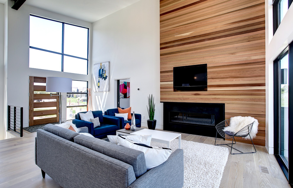Inspiration for a mid-sized contemporary formal open concept living room in Grand Rapids with white walls, light hardwood floors, a ribbon fireplace, a wall-mounted tv and a wood fireplace surround.