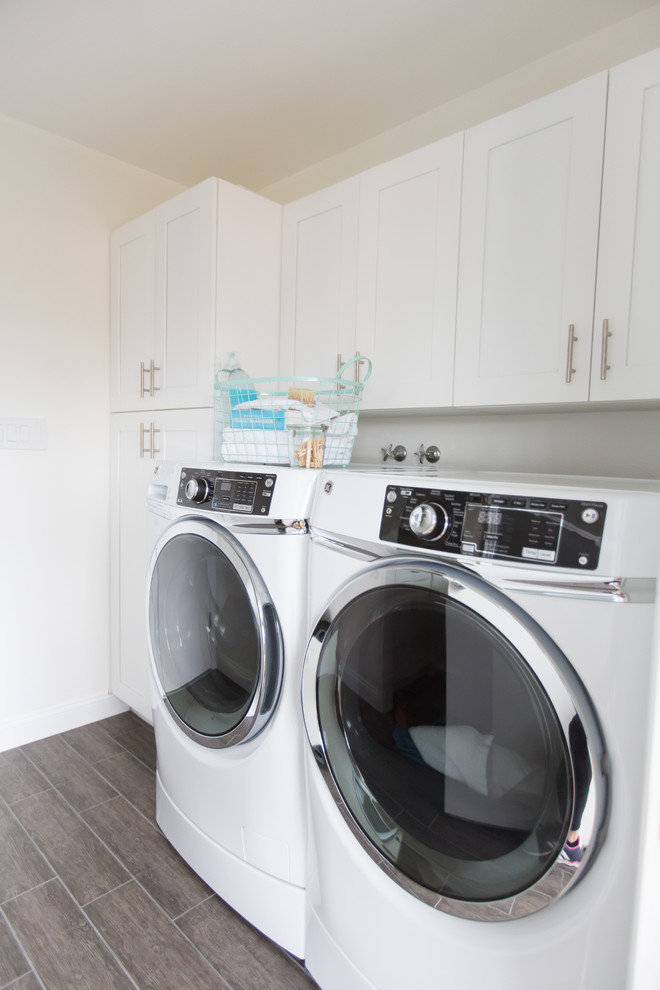 Photo of a mid-sized contemporary single-wall dedicated laundry room in Phoenix with a farmhouse sink, shaker cabinets, white cabinets, quartzite benchtops, white splashback, mosaic tile splashback, ceramic floors, white walls, a side-by-side washer and dryer and brown floor.