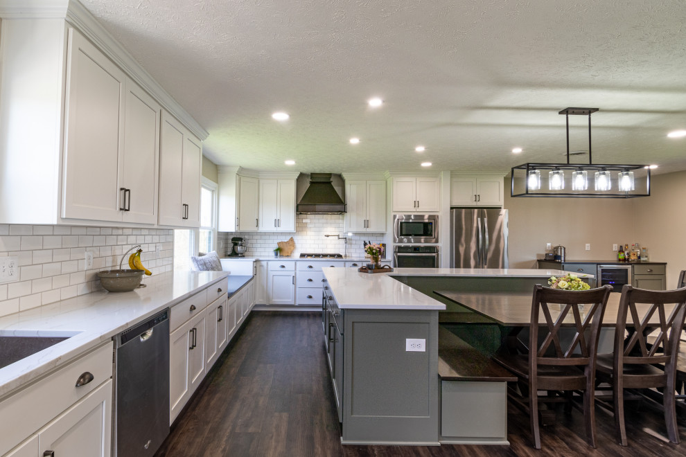 This is an example of an expansive rural l-shaped kitchen/diner in Cleveland with a submerged sink, shaker cabinets, green cabinets, engineered stone countertops, white splashback, metro tiled splashback, stainless steel appliances, vinyl flooring, an island, brown floors and white worktops.