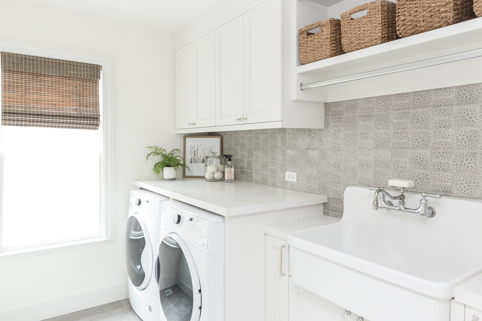 Photo of a transitional single-wall laundry room in San Francisco with an utility sink, shaker cabinets, white cabinets, white walls, a side-by-side washer and dryer, grey floor and white benchtop.