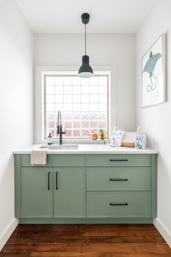 Inspiration for a mid-sized transitional galley laundry room in Vancouver with an undermount sink, shaker cabinets, green cabinets, quartz benchtops, white splashback, ceramic splashback, medium hardwood floors, brown floor, white benchtop and vaulted.