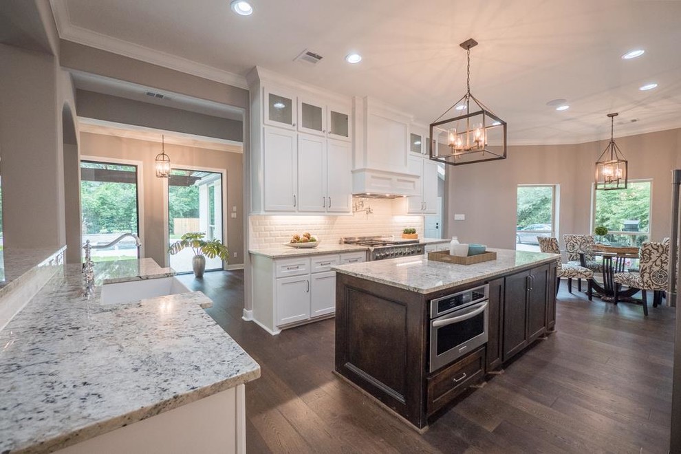 Photo of a large transitional u-shaped eat-in kitchen in Houston with a farmhouse sink, shaker cabinets, white cabinets, granite benchtops, white splashback, porcelain splashback, stainless steel appliances, medium hardwood floors and with island.
