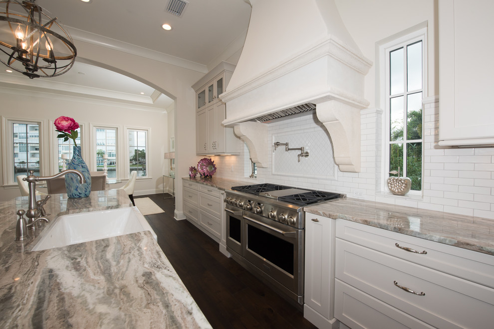 Photo of a large transitional galley eat-in kitchen in Tampa with a farmhouse sink, shaker cabinets, white cabinets, granite benchtops, white splashback, subway tile splashback, stainless steel appliances, dark hardwood floors and multiple islands.