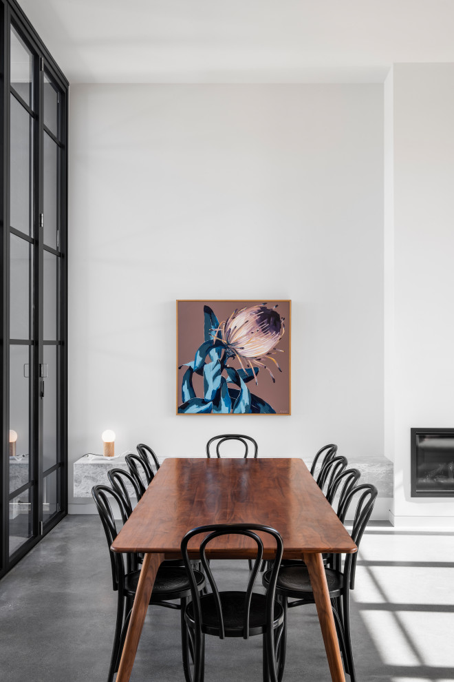 Cette photo montre une salle à manger ouverte sur le salon tendance de taille moyenne avec un mur blanc, sol en béton ciré, aucune cheminée, un manteau de cheminée en métal et un sol gris.