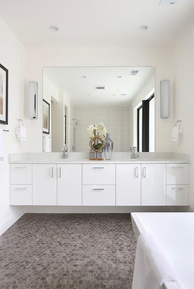 Mid-sized contemporary master bathroom in Denver with flat-panel cabinets, white cabinets, a freestanding tub, a shower/bathtub combo, white tile, ceramic tile, pebble tile floors, an undermount sink and engineered quartz benchtops.