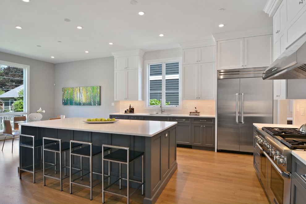 Example of a large transitional l-shaped light wood floor open concept kitchen design in Chicago with a single-bowl sink, shaker cabinets, gray cabinets, quartzite countertops, white backsplash, ceramic backsplash, stainless steel appliances and an island
