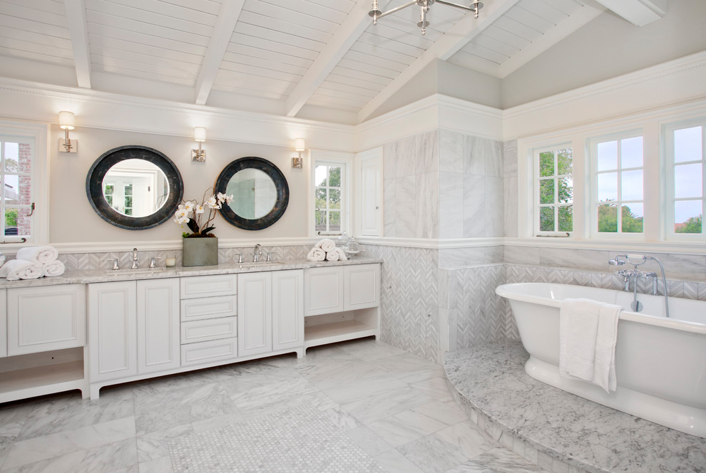 Inspiration for a large transitional master bathroom in Los Angeles with recessed-panel cabinets, white cabinets, a freestanding tub, an alcove shower, a one-piece toilet, white tile, marble, grey walls, marble floors, an undermount sink, marble benchtops, grey floor, a hinged shower door and white benchtops.