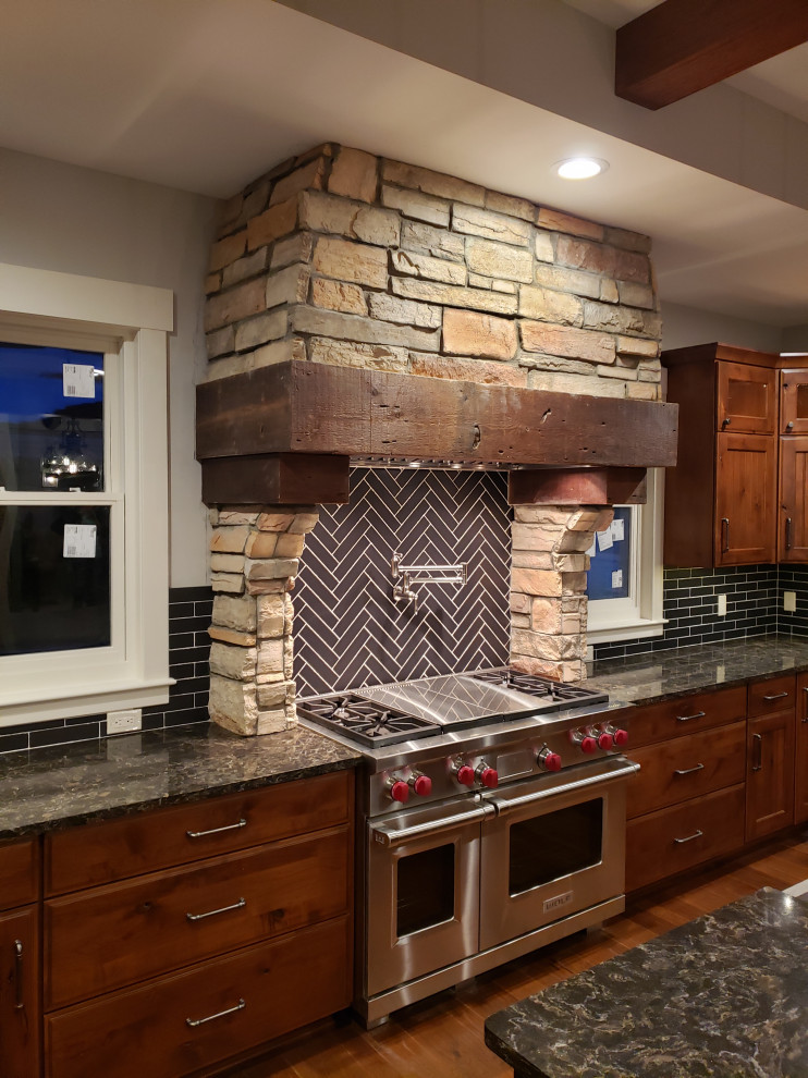Kitchen - rustic medium tone wood floor kitchen idea in Grand Rapids with a farmhouse sink, recessed-panel cabinets, dark wood cabinets, quartz countertops, black backsplash, travertine backsplash, stainless steel appliances, an island and brown countertops