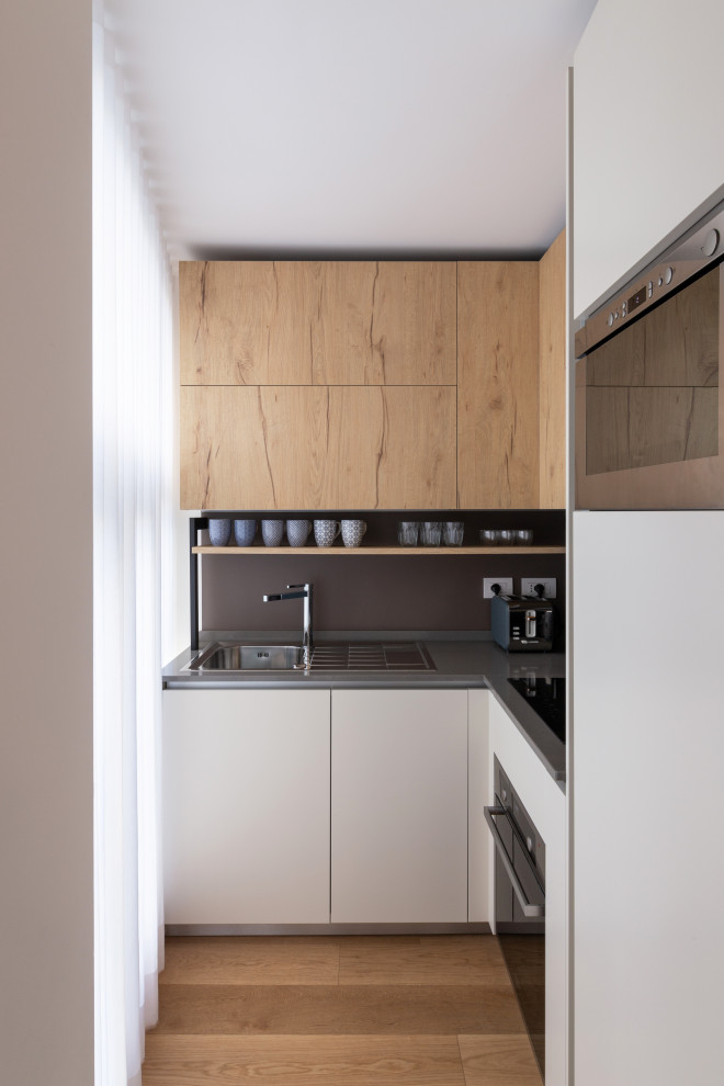 Moderne Küche in L-Form mit Einbauwaschbecken, flächenbündigen Schrankfronten, Küchenrückwand in Grau, grauer Arbeitsplatte und hellem Holzboden in Mailand