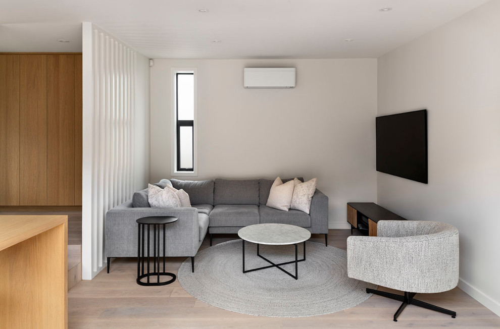 This is an example of a mid-sized contemporary enclosed living room in Auckland with white walls, light hardwood floors, a wall-mounted tv, beige floor and panelled walls.