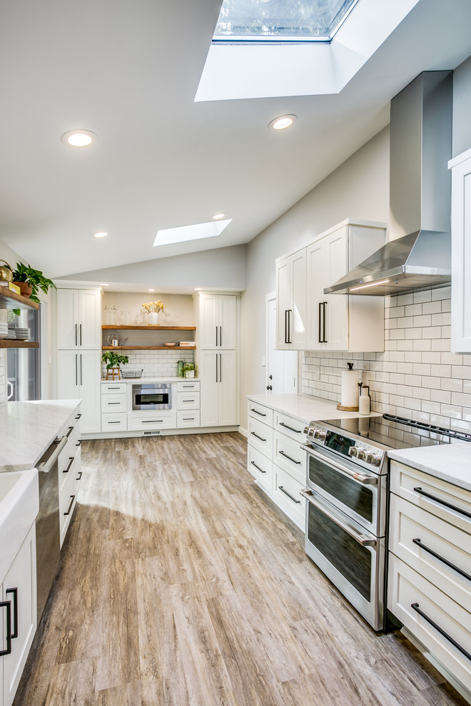 This is an example of a mid-sized transitional galley kitchen pantry in Seattle with a farmhouse sink, shaker cabinets, white cabinets, marble benchtops, white splashback, subway tile splashback, stainless steel appliances, laminate floors, no island, brown floor and white benchtop.
