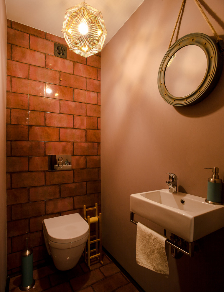 Inspiration for a small industrial powder room in Other with a wall-mount toilet, red tile, ceramic tile, pink walls, porcelain floors and a wall-mount sink.