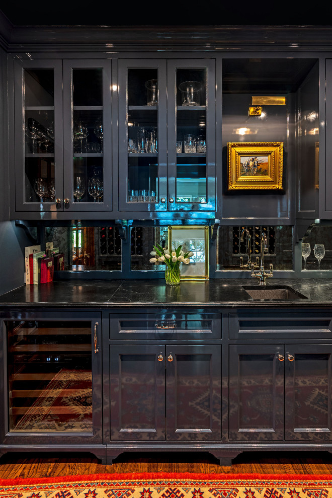 Photo of a mid-sized traditional galley wet bar in Houston with an undermount sink, beaded inset cabinets, blue cabinets, soapstone benchtops, mirror splashback, dark hardwood floors, brown floor and black benchtop.