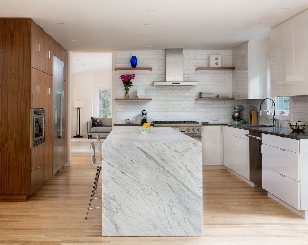 Design ideas for a large contemporary l-shaped eat-in kitchen in Denver with an undermount sink, flat-panel cabinets, white cabinets, marble benchtops, white splashback, glass tile splashback, stainless steel appliances, light hardwood floors and with island.