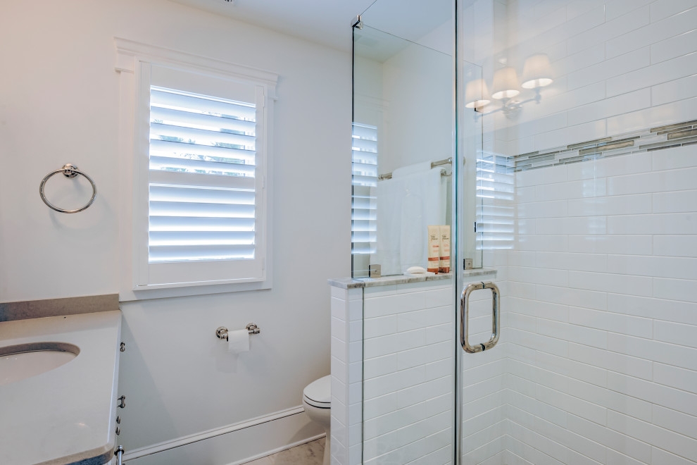 This is an example of a mid-sized beach style 3/4 bathroom in Other with recessed-panel cabinets, white cabinets, a corner shower, a two-piece toilet, white tile, subway tile, white walls, granite benchtops and a hinged shower door.