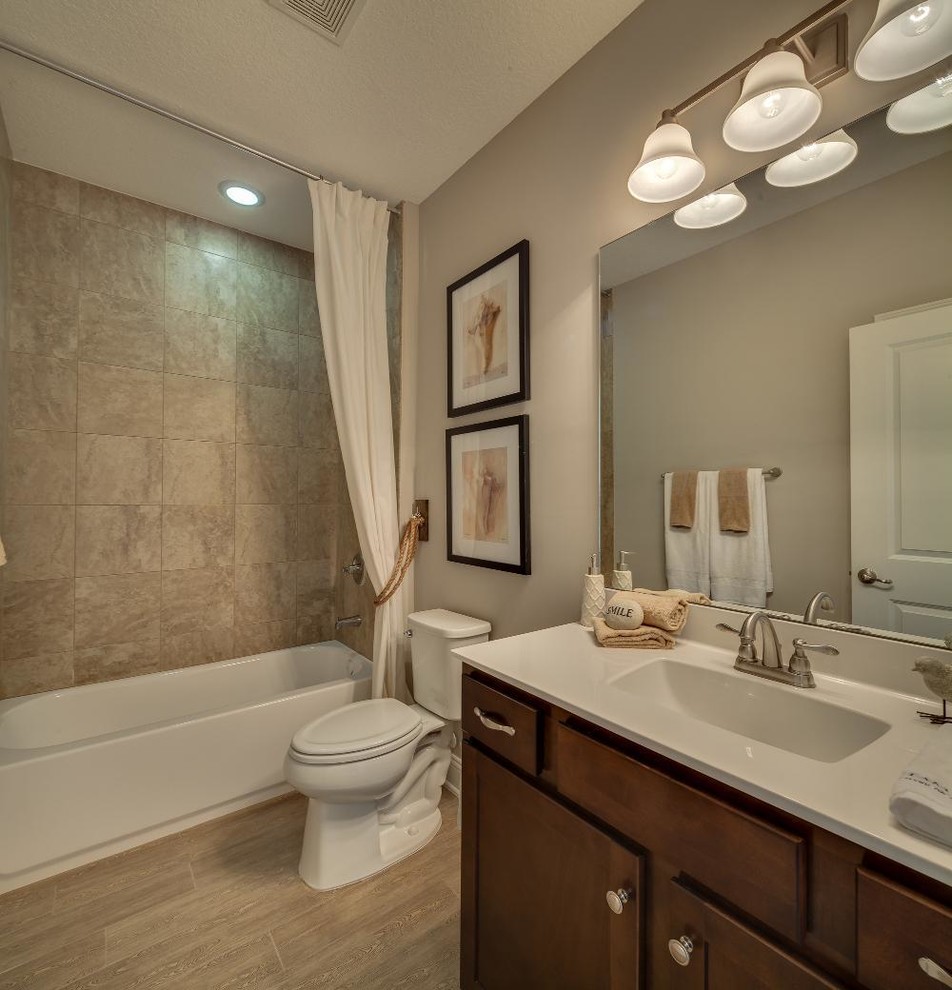 Design ideas for a mid-sized traditional 3/4 bathroom in Jacksonville with shaker cabinets, medium wood cabinets, an alcove tub, a shower/bathtub combo, a two-piece toilet, beige walls, laminate floors, an undermount sink, solid surface benchtops and a shower curtain.