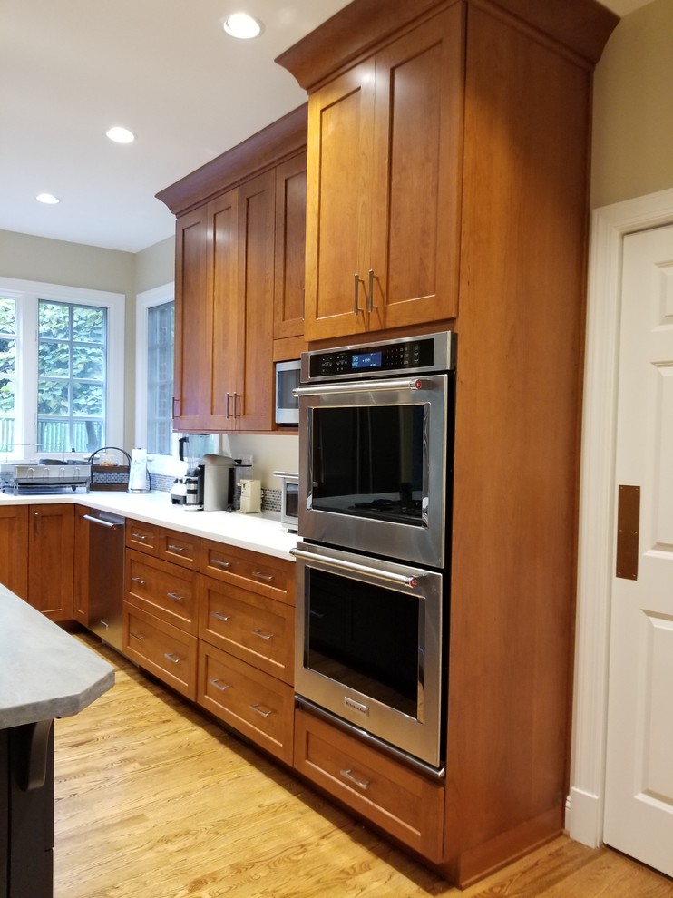 Inspiration for a mid-sized transitional l-shaped eat-in kitchen in DC Metro with an integrated sink, recessed-panel cabinets, medium wood cabinets, solid surface benchtops, blue splashback, mosaic tile splashback, stainless steel appliances, medium hardwood floors, a peninsula, brown floor and blue benchtop.