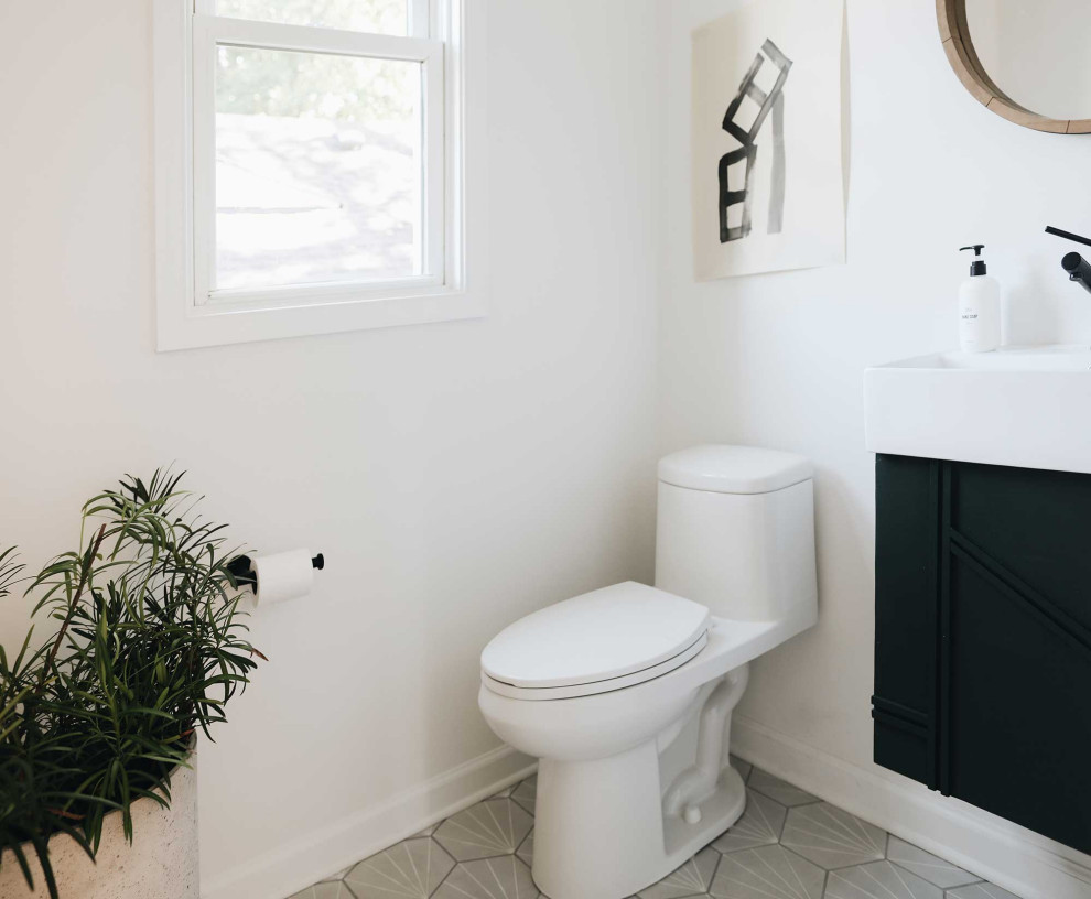 50 tals inredning av ett litet badrum med dusch, med gröna skåp, en toalettstol med hel cisternkåpa, vita väggar, cementgolv, ett väggmonterat handfat och grått golv