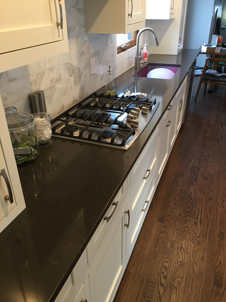 Example of a large transitional dark wood floor and brown floor kitchen design in Minneapolis with an undermount sink, shaker cabinets, white cabinets, quartzite countertops, gray backsplash, stone tile backsplash, stainless steel appliances and an island