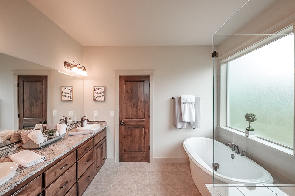 This is an example of a master wet room bathroom in Portland with raised-panel cabinets, medium wood cabinets, a freestanding tub, beige walls, a drop-in sink, granite benchtops, beige floor, a hinged shower door, multi-coloured benchtops, multi-coloured tile and matchstick tile.