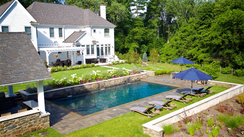 Inspiration for a large traditional backyard rectangular lap pool in Philadelphia with a water feature and concrete pavers.