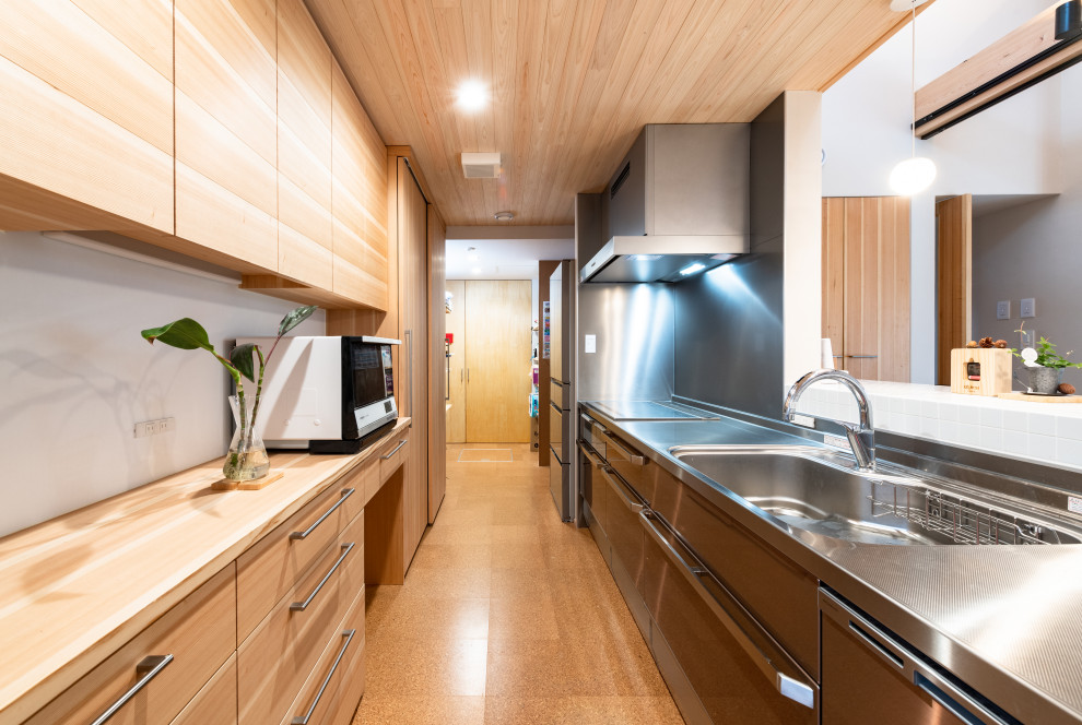 This is an example of a mid-sized asian single-wall separate kitchen in Other with an integrated sink, flat-panel cabinets, light wood cabinets, stainless steel benchtops, metallic splashback, panelled appliances, cork floors and wood.