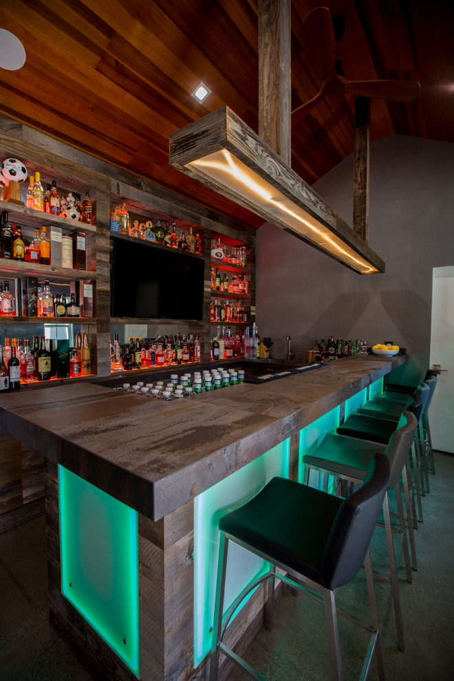 This is an example of a mid-sized industrial u-shaped seated home bar in San Francisco with an undermount sink, open cabinets, distressed cabinets, concrete benchtops, timber splashback, concrete floors, grey floor and grey benchtop.